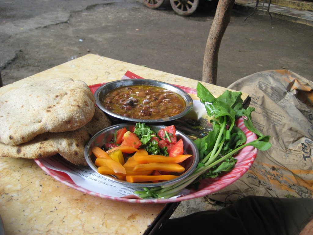 Ful medames servido en un puesto callejero de El Cairo con pan, encurtidos y hojas frescas