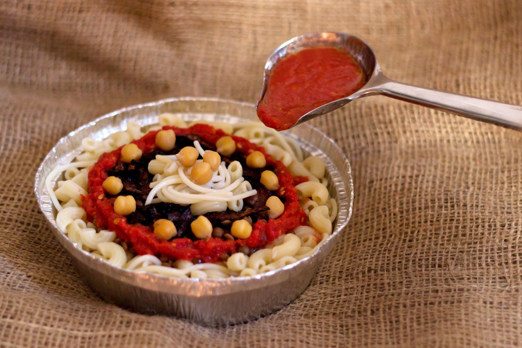 Plato de koshary egipcio con arroz, pasta, lentejas, garbanzos y cebolla frita